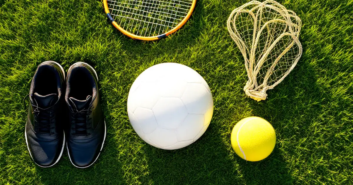 Sports equipment on a Surrey grass pitch — football, tennis racket, netball and cricket bat all fully visible, summer holiday camps Surrey
